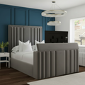 Gray upholstered bed in a bedroom setting with a television and decor elements.